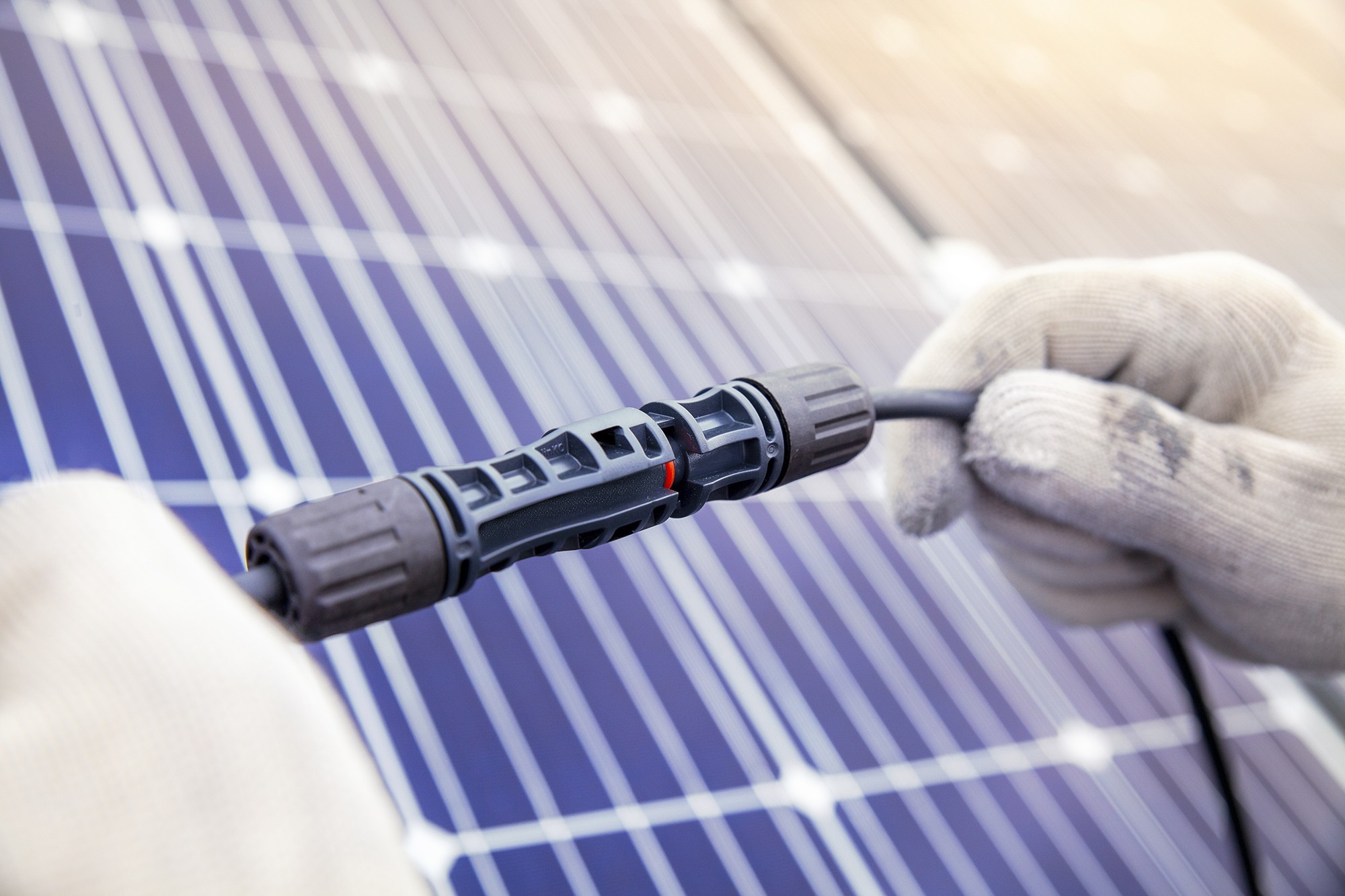 Gloved hands manipulating a connector in front of a solar panel.