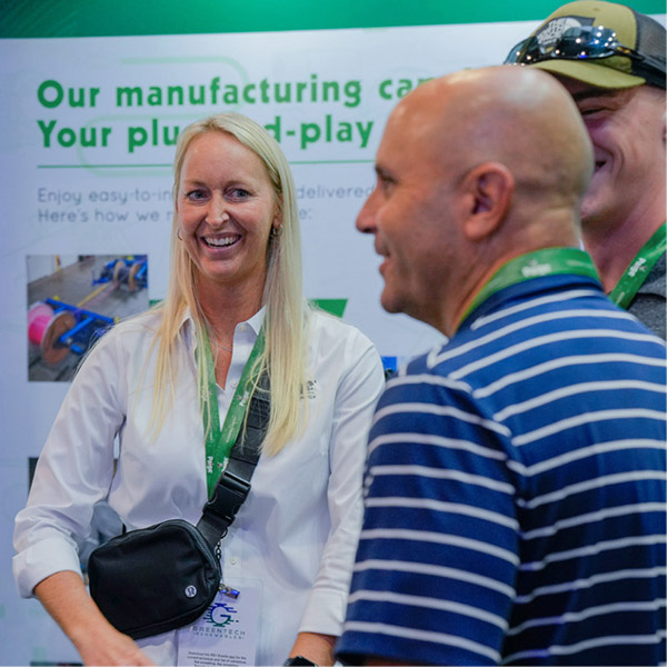 Three tradeshow attendees engage in conversation in front of a Paige Renewable Energy banner.