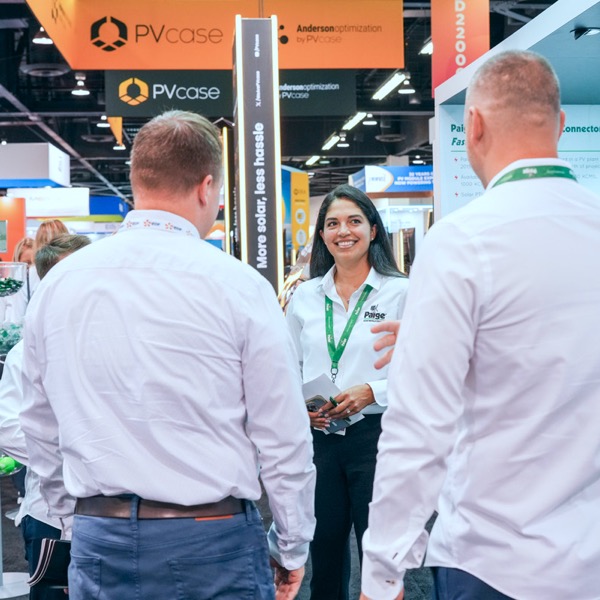 Three tradeshow attendees engage in conversation in front of a Paige Renewable Energy banner.